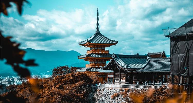 Eine mehrstöckige Pagode des Kiyomizu-dera Tempels überblickt Kyoto mit bewaldeten Hügeln und der Stadt in der Ferne darunter.