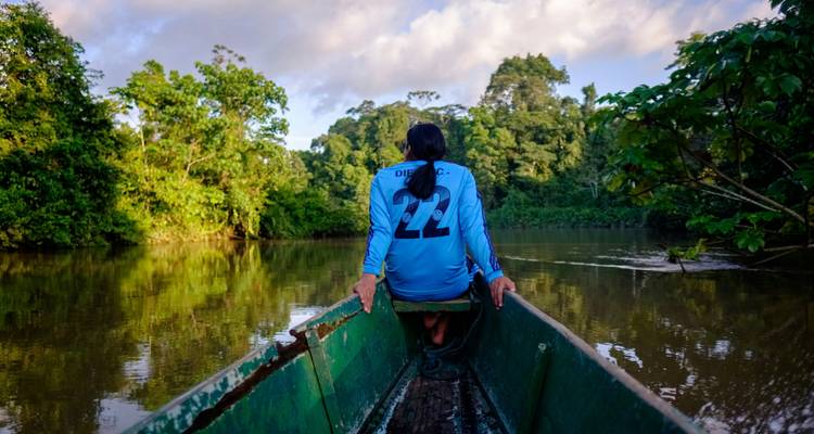 Personne dans un bateau sur une rivière entourée d'une jungle dense.