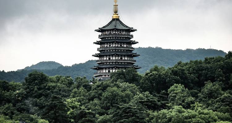 Pagode s'élevant au-dessus d'une colline boisée sous un ciel nuageux.