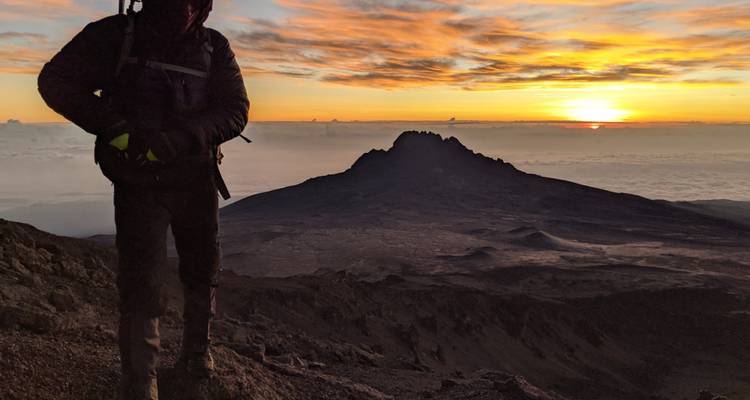 Excursionista silueteado contra un amanecer sobre una montaña.