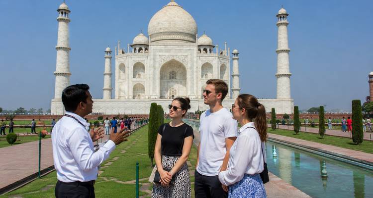 Guía local explicando la historia a cuatro viajeros frente al Taj Mahal en un día soleado.