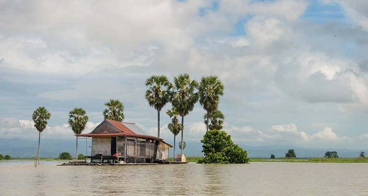 Maison en bois sur pilotis entourée de palmiers située sur un lac tranquille sous un ciel nuageux à Sulawesi.