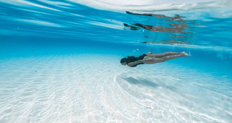 Person, die unter Wasser in klarem blauen Wasser schwimmt.
