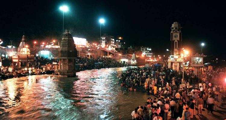 Scène nocturne animée au bord d'une rivière avec des temples et des lumières.