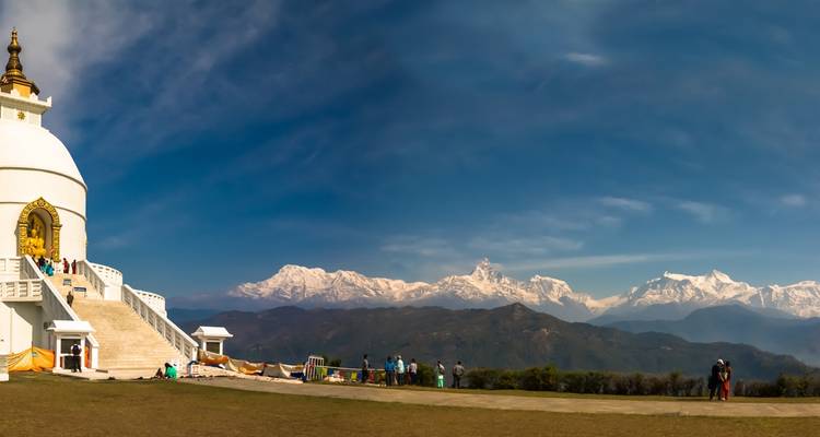 Grand stupa avec des gens autour, montagnes en arrière-plan.