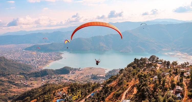 Parapentistes planant au-dessus d'un lac et de montagnes, avec une vue panoramique sur la ville.