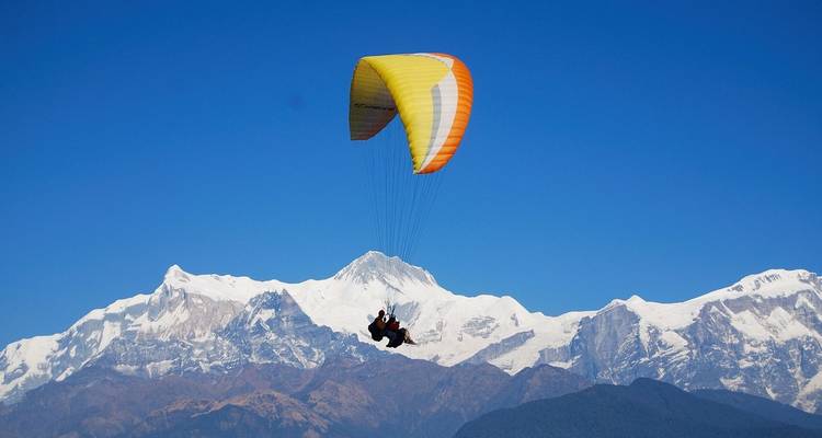Parapentiste avec des sommets montagneux enneigés en arrière-plan.