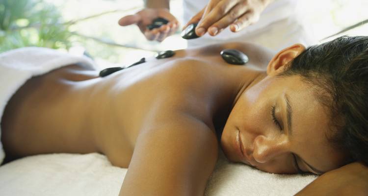 Ein Therapeut platziert warme Steine entlang des Rückens einer Frau während einer entspannenden Spa-Behandlung.