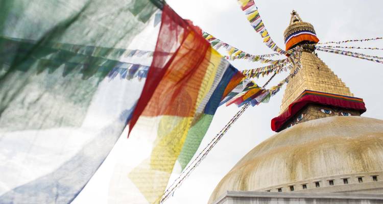 Las banderas de oración ondean alrededor de una cúpula de estupa de techo dorado bajo cielos brillantes.
