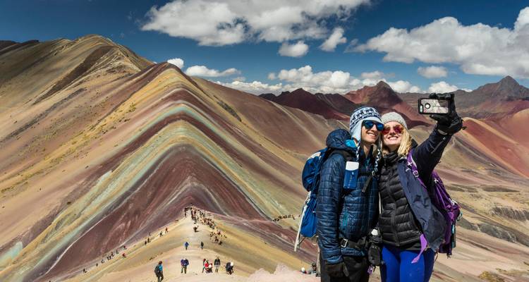 Twee mensen die een selfie maken met Rainbow Mountain op de achtergrond.