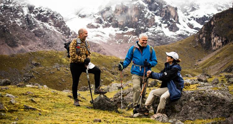 Drie mensen die wandelen in een bergachtig gebied met besneeuwde toppen.