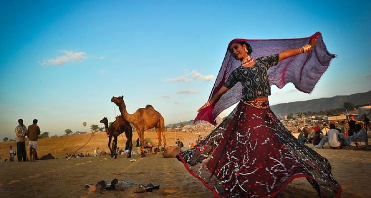 Danseuse se produisant dans le désert avec des chameaux et des gens.