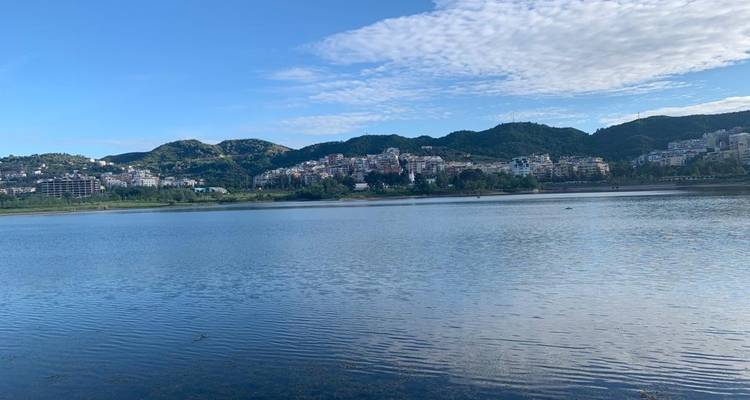 Kalm meer met heuvels en gebouwen op de achtergrond onder een blauwe hemel.