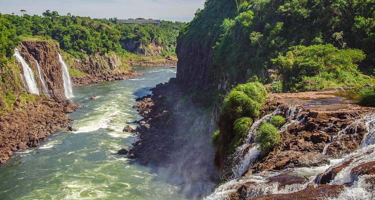 Rivierkloof bij Iguazu met meerdere watervallen die vanaf beboste kliffen naar beneden storten onder helder licht.