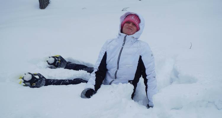Personne assise dans la neige profonde portant des vêtements d'hiver, souriante.