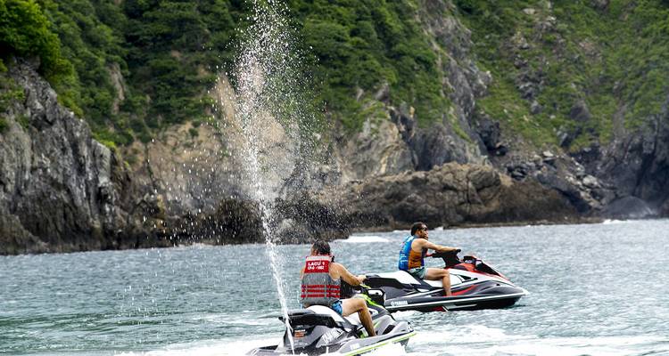 Deux personnes sur des jet-skis avec des falaises luxuriantes en arrière-plan.