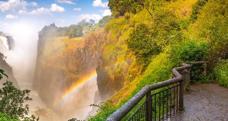 Victoria Falls met een regenboog en nevel die oprijst van de waterval.