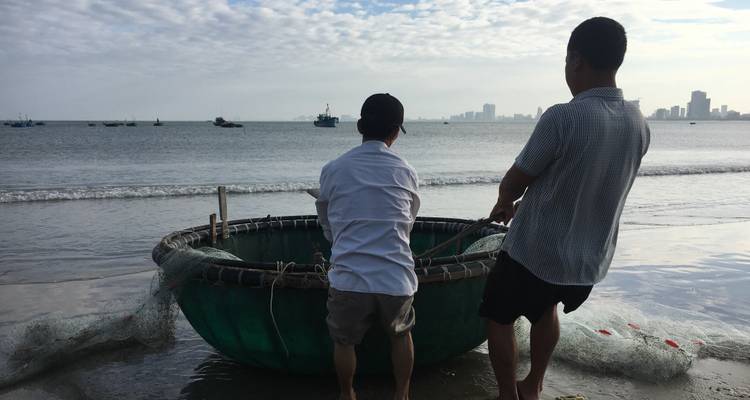 Two people with a round basket boat on a beach.