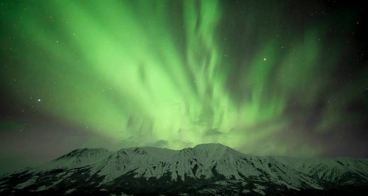 Briljantgroene aurora verspreidt zich als vlammen boven besneeuwde bergketen