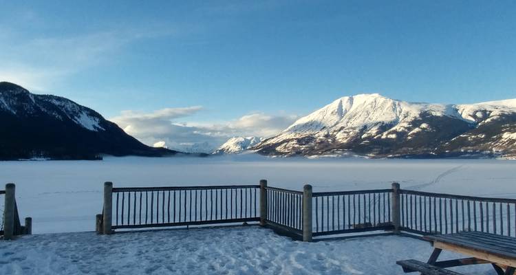 Houten terras kijkt uit over bevroren meer en besneeuwde bergen onder blauwe lucht