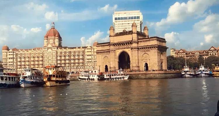 Blick auf das Gateway of India mit Booten und einem historischen Hotel im Hintergrund.