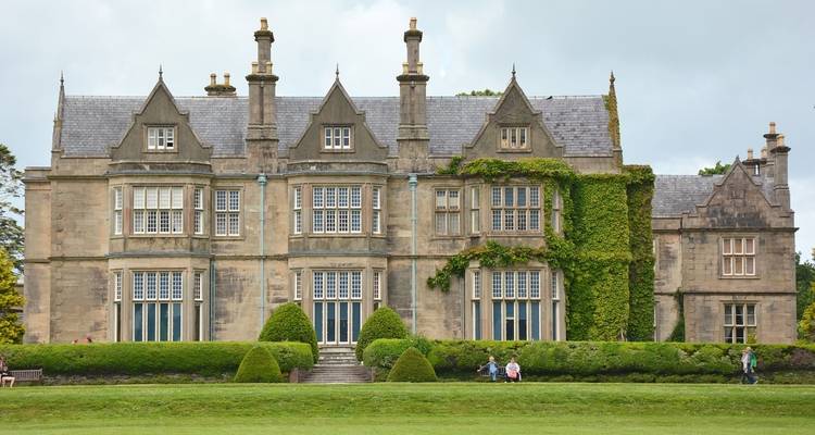 Demeure majestueuse avec jardins entretenus et des gens sur la pelouse.