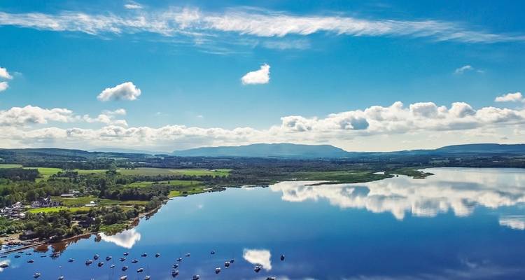 Vista aérea de un lago reflectante con botes y el paisaje circundante.