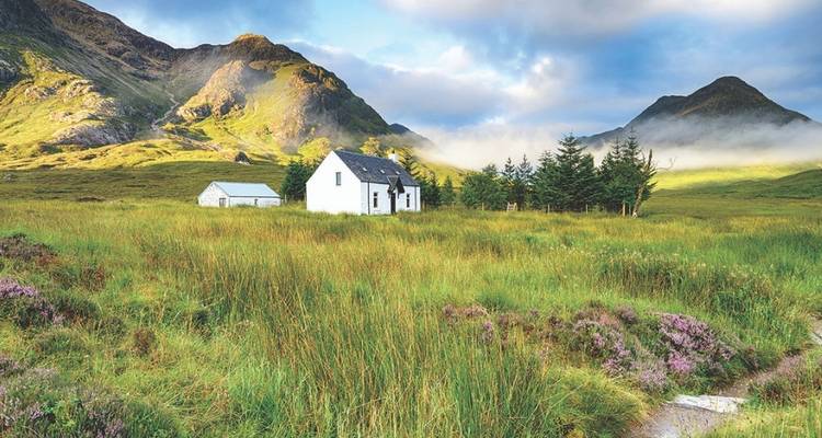 Cottage in a grassy valley surrounded by mountains.