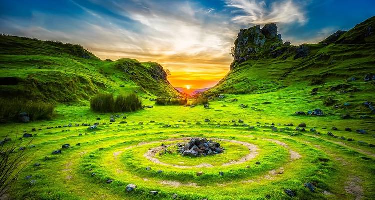 Vallée verte avec un cercle de pierres sous un coucher de soleil vibrant.