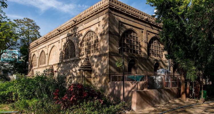 Historisches Gebäude mit kunstvollen Steinfenstern, umgeben von Grün.