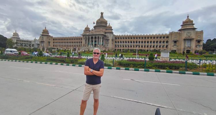 Mann posiert vor Vidhana Soudha an einem bewölkten Tag.