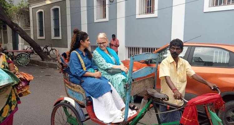 Deux femmes assises dans un pousse-pousse avec un homme debout à côté.