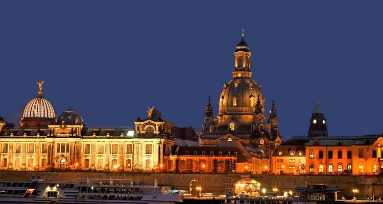 Nächtliche Ansicht der beleuchteten Dresdner Frauenkirche und Uferbebauung unter klarem Himmel.