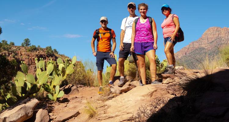 Groupe de randonneurs posant sur un sentier rocheux avec des montagnes en arrière-plan.