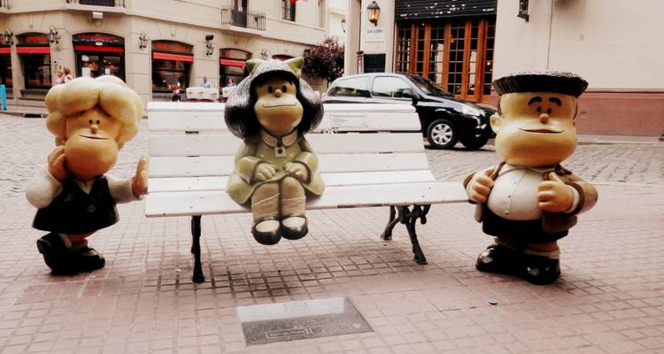 Statues of cartoon characters on a bench in a city street.