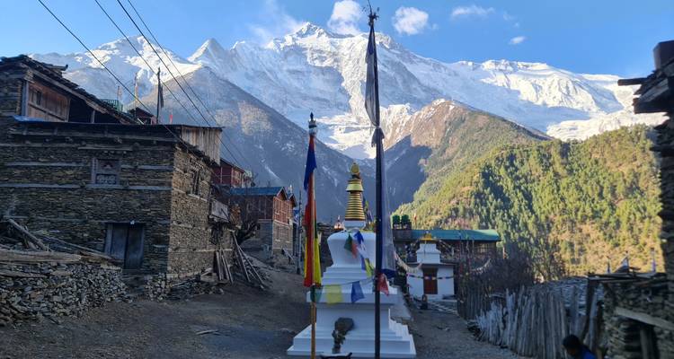 Ein kleines himalayisches Dorf mit einem Chorten und wehenden Gebetsfahnen liegt unterhalb von aufragenden Schneebergen.