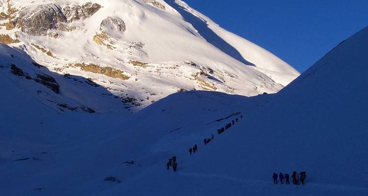 Fila de excursionistas en un sendero de montaña nevado.