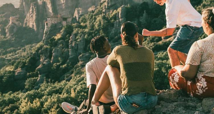 Los viajeros se sientan en el borde de un acantilado con vistas a los impresionantes monasterios de roca de Meteora al atardecer.