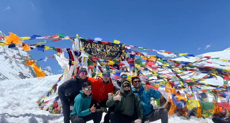 Les trekkers posent avec les pouces levés devant les drapeaux de prière colorés et le panneau du col enneigé de Larke.