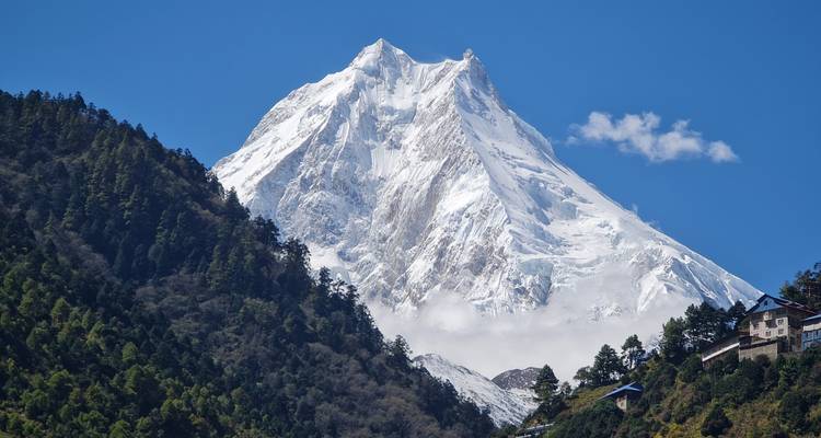 Un impressionnant pic pyramidal blanc s'élève au-dessus de crêtes forestières sombres par une journée cristalline.