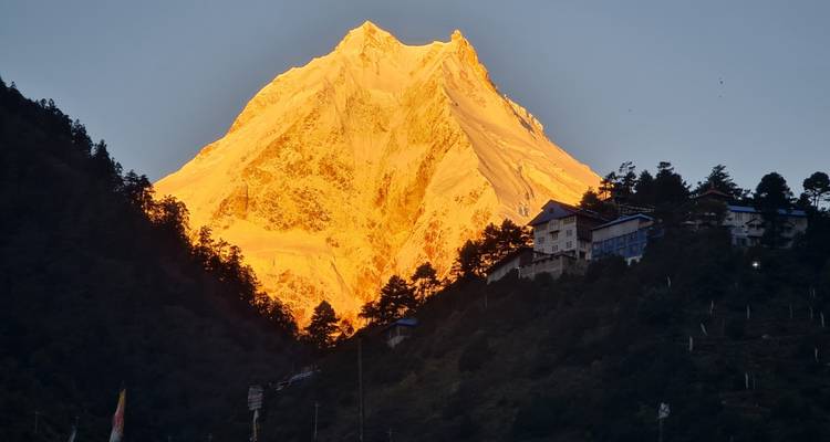 La lueur alpestre du coucher de soleil embrase un pic enneigé d'une lumière dorée au-dessus de collines sombres.