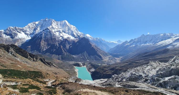 Vaste panorama alpin avec lac glaciaire turquoise, chaînes de montagnes enneigées aux crêtes déchiquetées et vallée sinueuse.