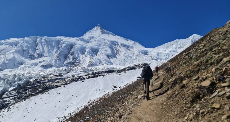 Les trekkeurs gravissent un sentier étroit et enneigé sous un sommet imposant recouvert de glacier.