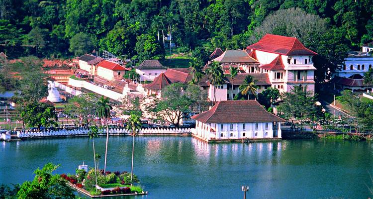 Lago pintoresco rodeado de templos y edificios con techos rojos contra colinas exuberantes.