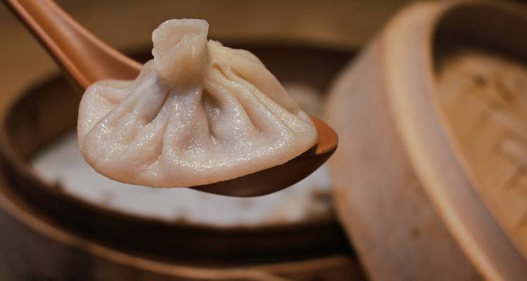 Primer plano de un dumpling de sopa humeante levantado en una cuchara de madera