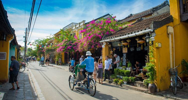 Farbenfrohe Straße in der Altstadt von Hoi An mit Bougainvillea und einem Cyclo-Fahrer.