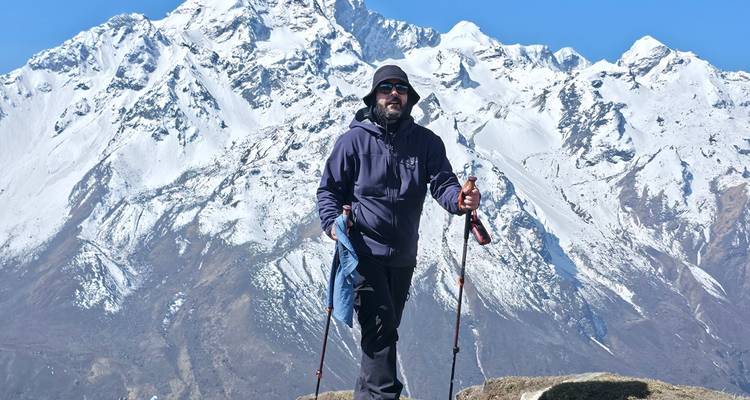 Solo trekker stands on a rock with snow-covered Langtang peaks towering behind.