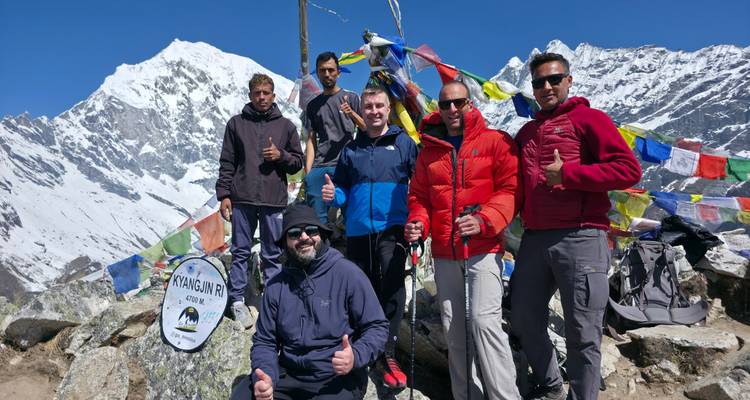 Small trekking group poses with prayer flags at Kyangjin Ri viewpoint against snowy summits.