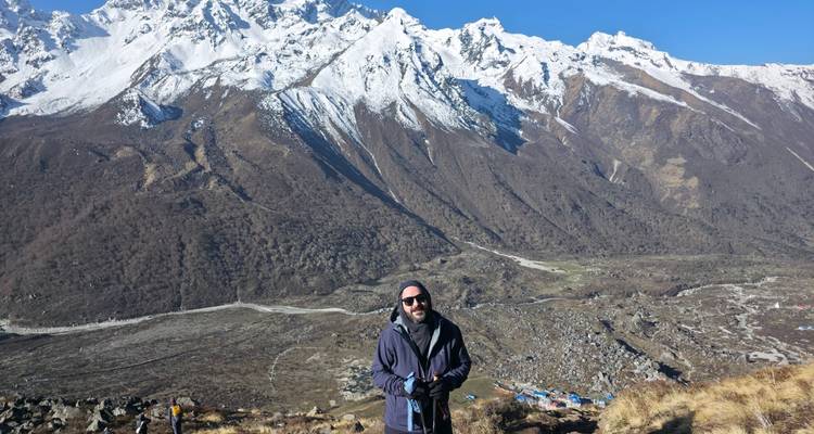 Trekker enjoys a panoramic Himalayan valley vista with winding river far below.