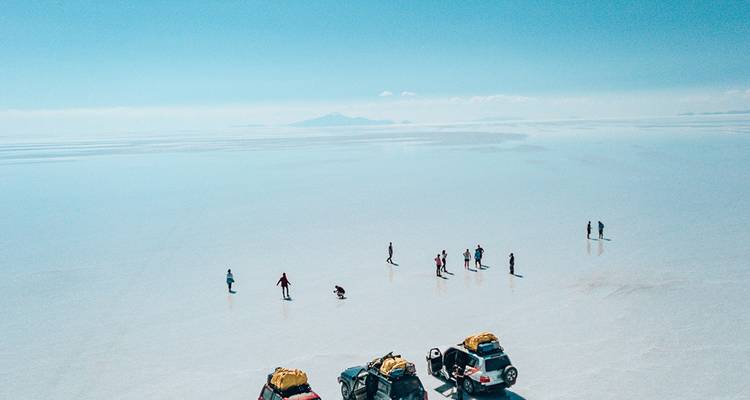 Vue aérienne de jeeps et de visiteurs éparpillés sur la vaste étendue blanche des salines d'Uyuni s'étendant jusqu'à l'horizon.